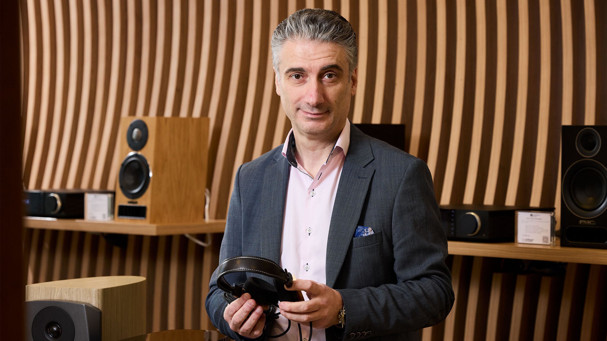 photo-man-in-a-suit-holding-a-pair-of-headphones-with-audio-equipment-behind-him