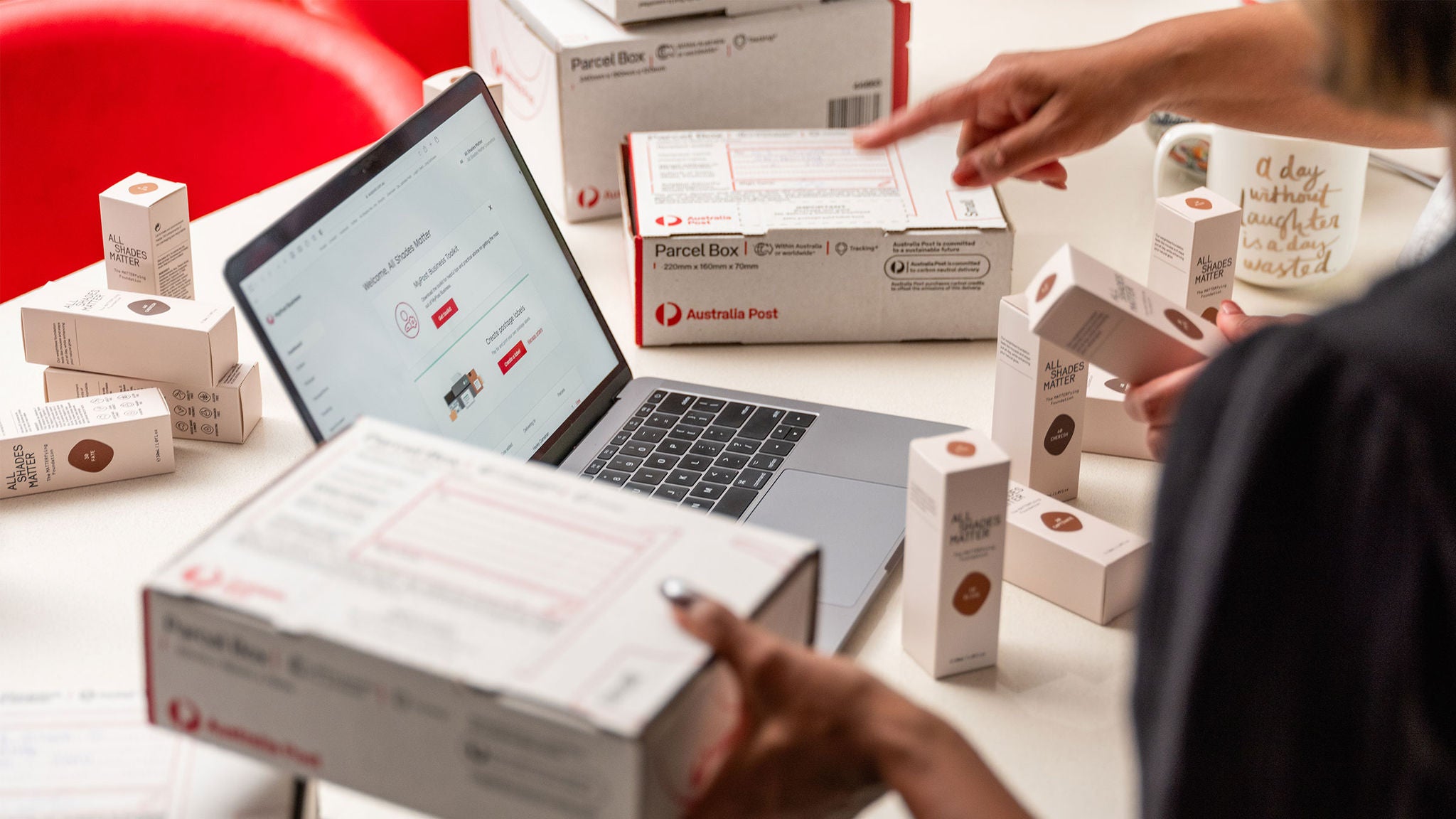 photo-close-up-of-a-table-full-of-make-up-products-and-austraila-post-boxes-and-a-laptop-with-screen-showing-mypost-business