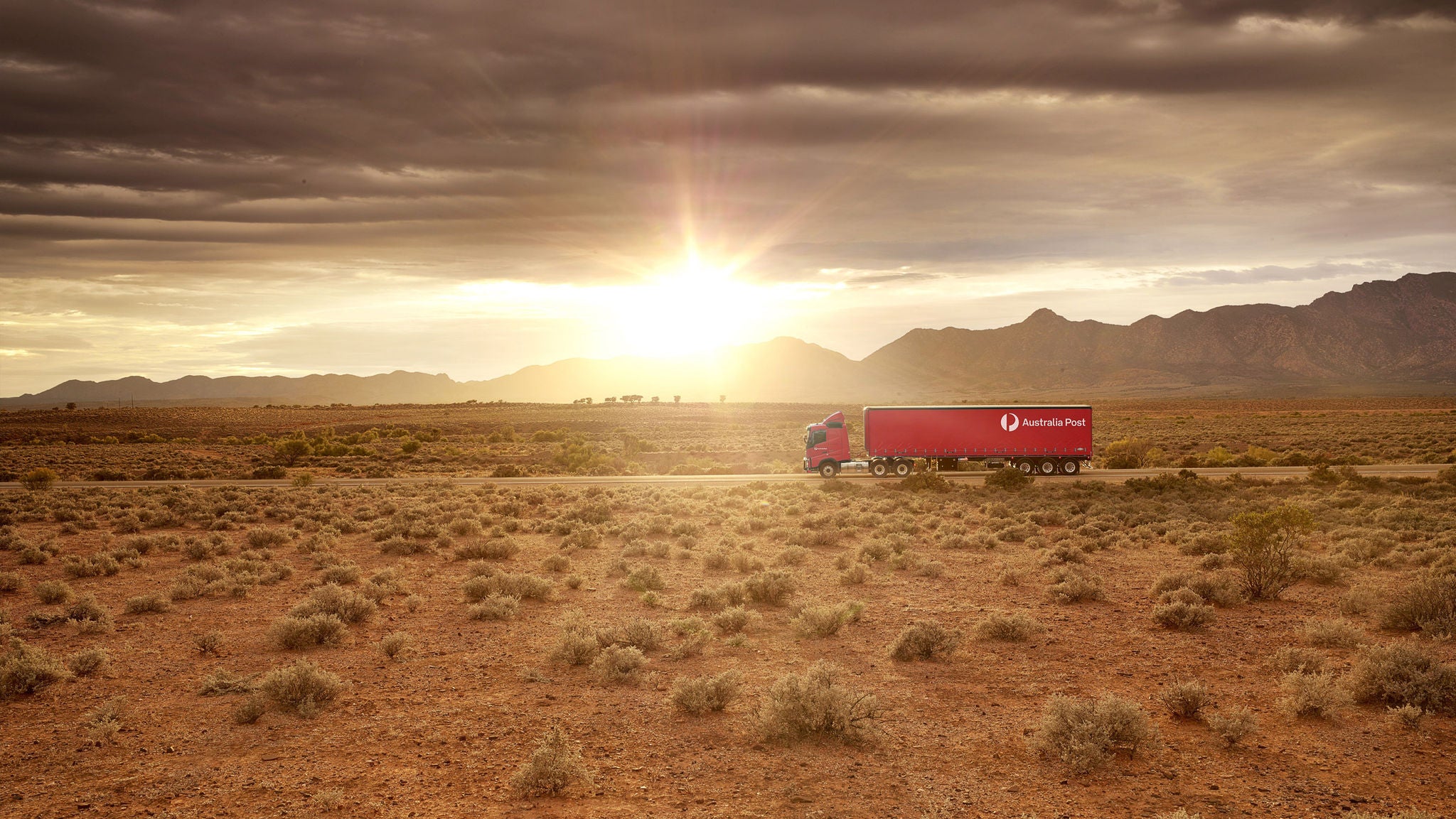A semi-trailer driving through the outback at sunrise