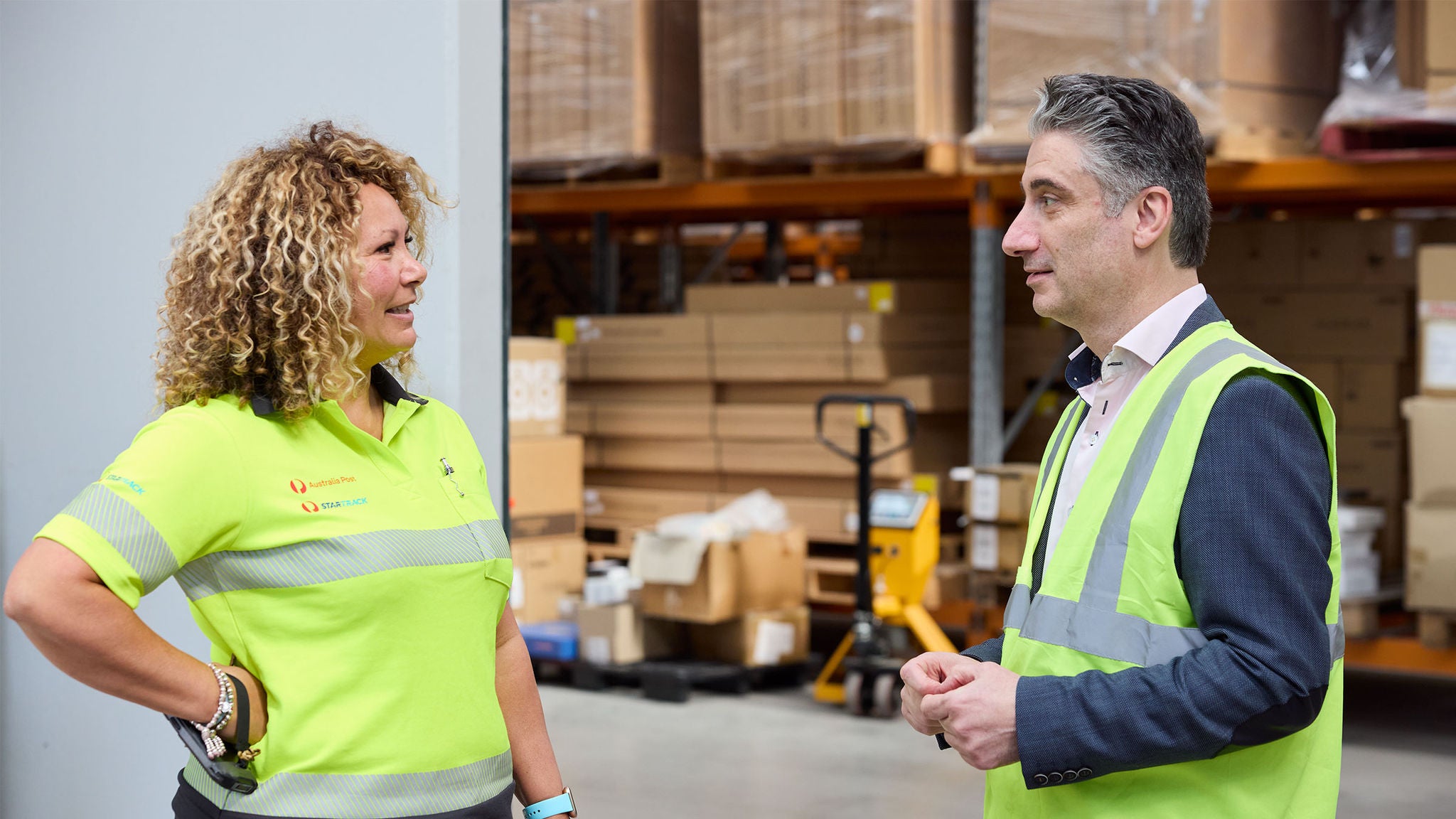 photo-female-startrack-driver-talking-to-a-man-wearing-a-high-vis-vest-in-a-warehouse