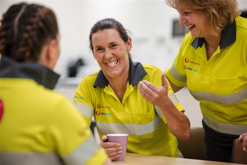 3 women in Network Operations uniform laughing around a lunch table