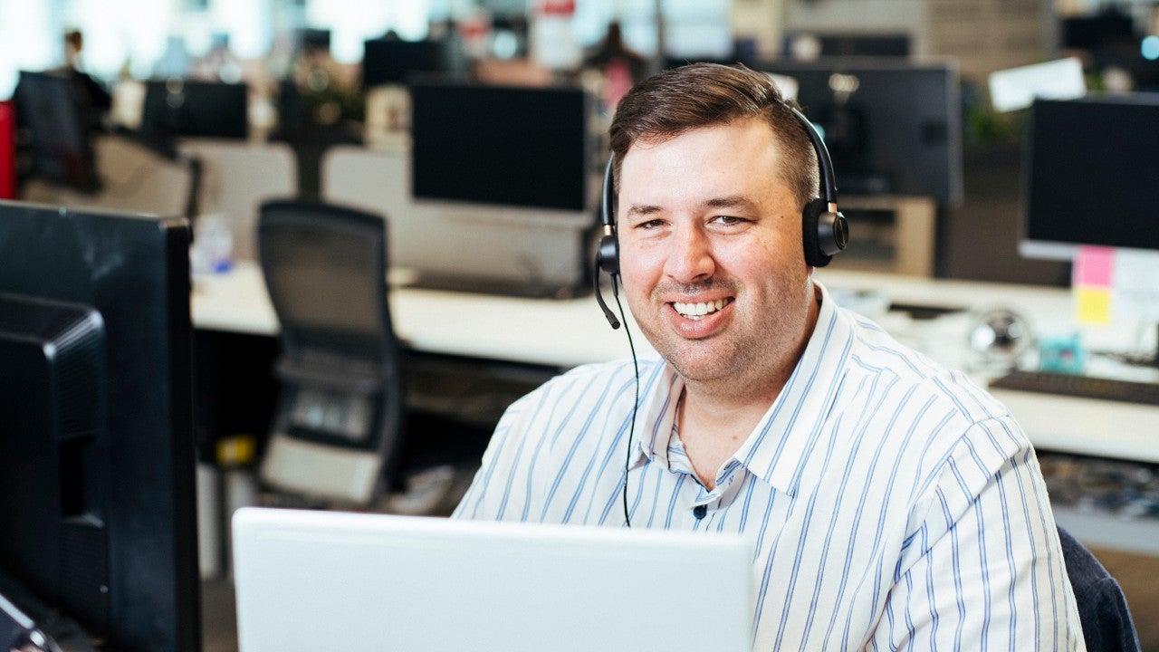 Man working in our call centre sitting at a desk with a headset on, smiling