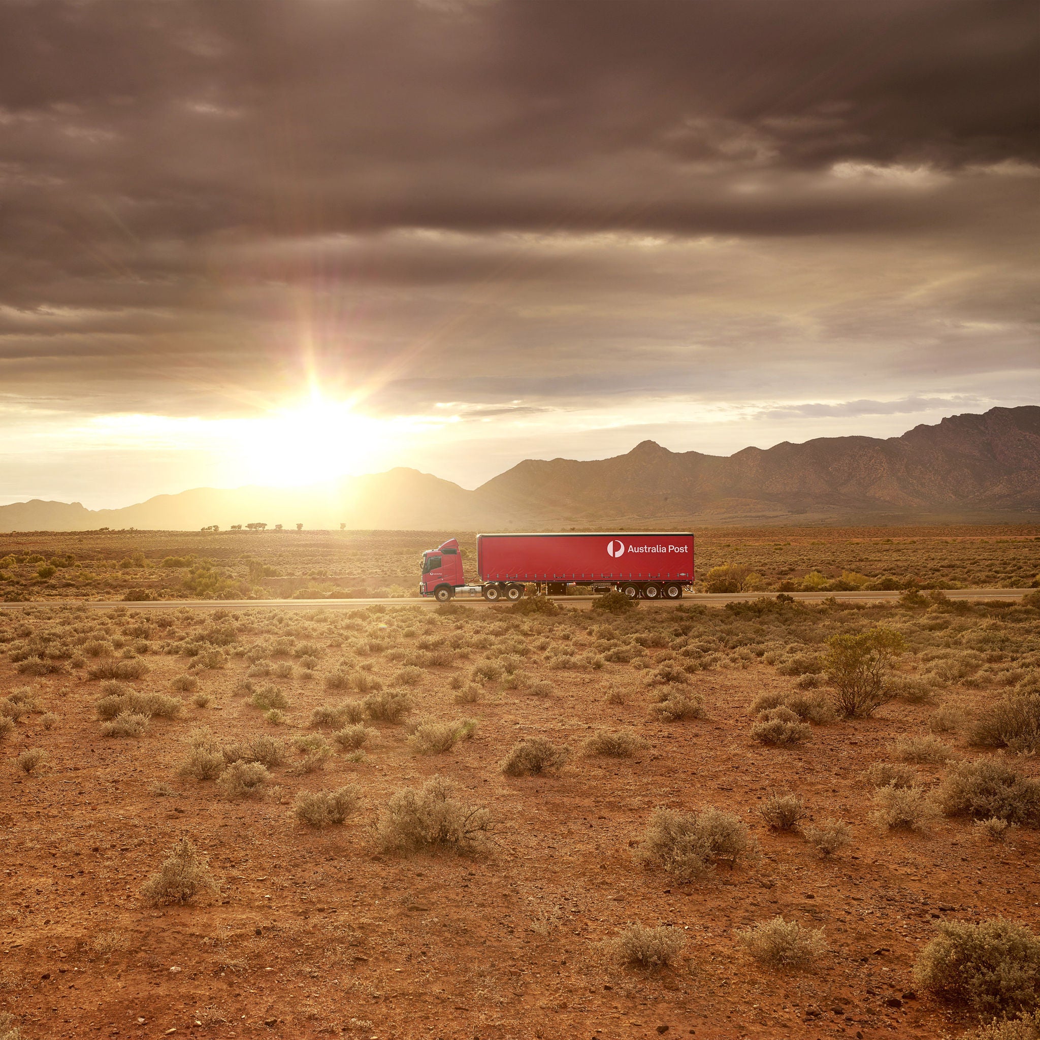A semi-trailer driving through the outback at sunrise