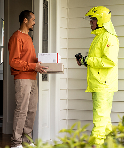 Man chatting and receiving two Australia Post parcels from postie at his home