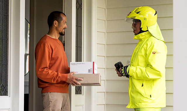 Man chatting and receiving two Australia Post parcels from postie at his home