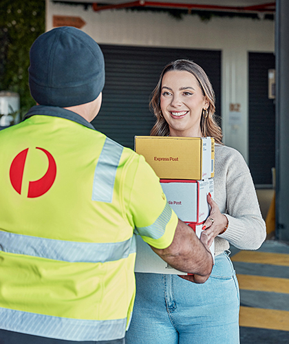 Woman receiving Australia Post boxes from postie in a warehouse